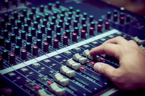 A recording studio mixing desk with the audio engineer's hand adjusting the faders to achieve the best possible result.